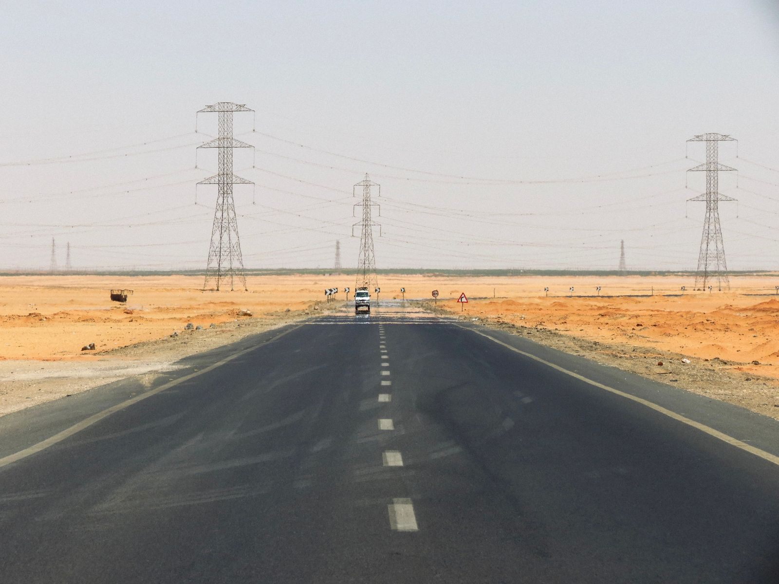 A straight two-lane highway across flat desert under power pylons; for a carful of people, driving is often the cheapest way to travel across the country