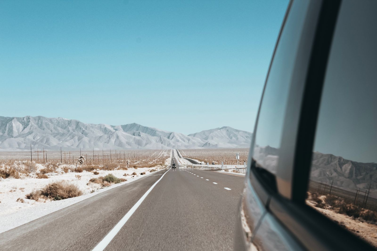 View from a car window of a straight road heading across desert toward snowy mountains